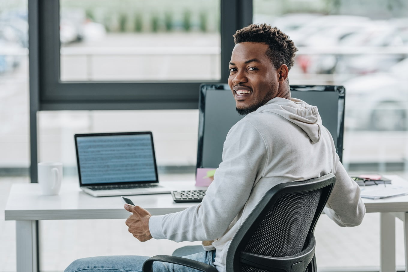 happy african american programmer smiling at camera while sitting at workplace in office